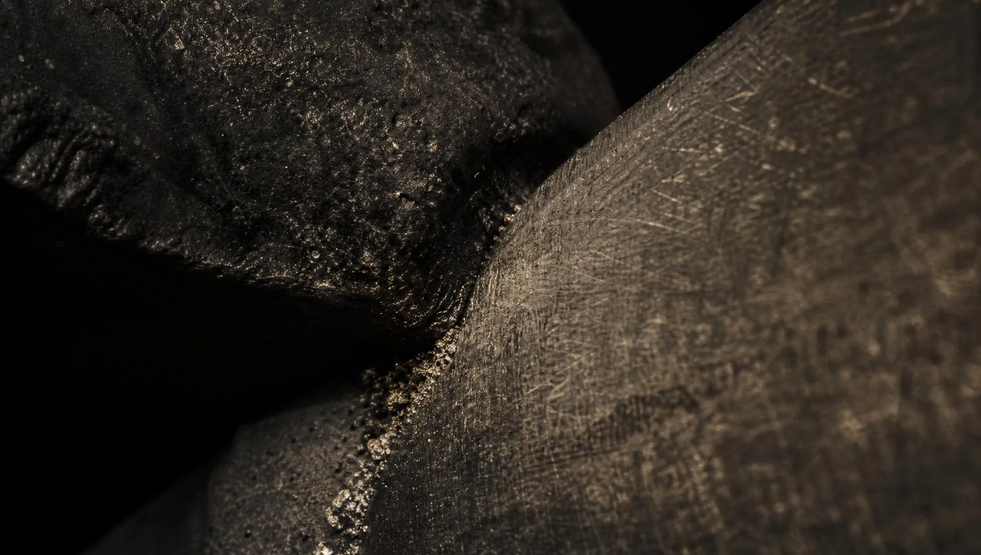 Two rough surfaces meeting under raking warm light, texture and grit at the contact line.