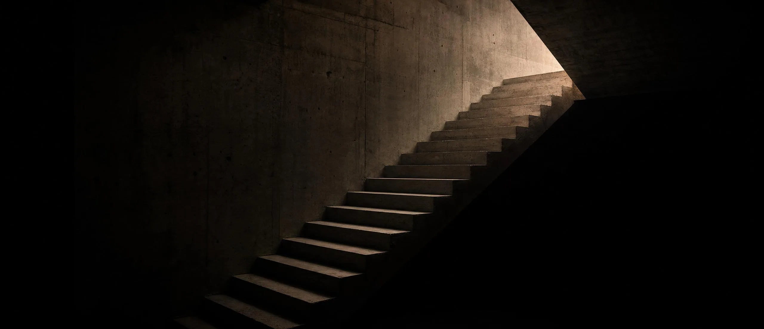 A concrete staircase rising through darkness toward a single warm light above.