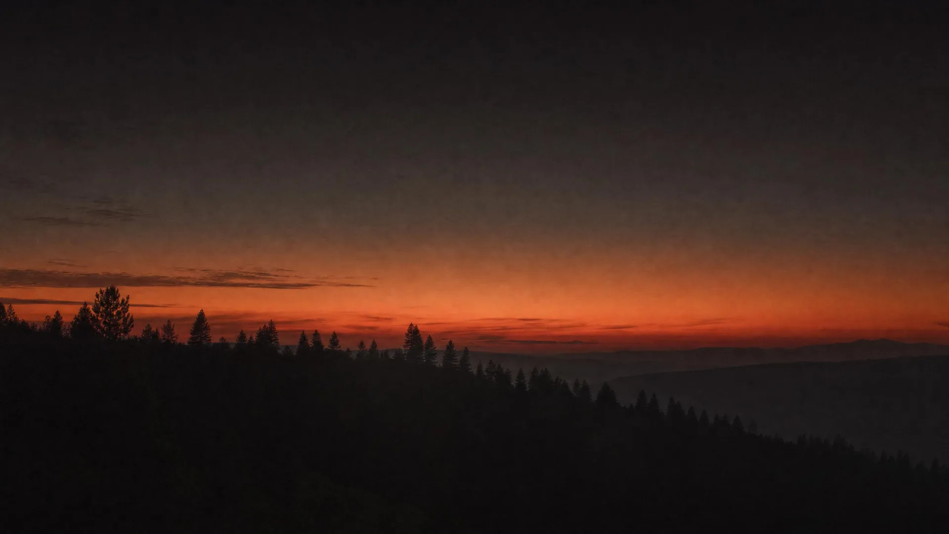 Silhouetted pines under a brick-red and amber Inland Northwest dusk.